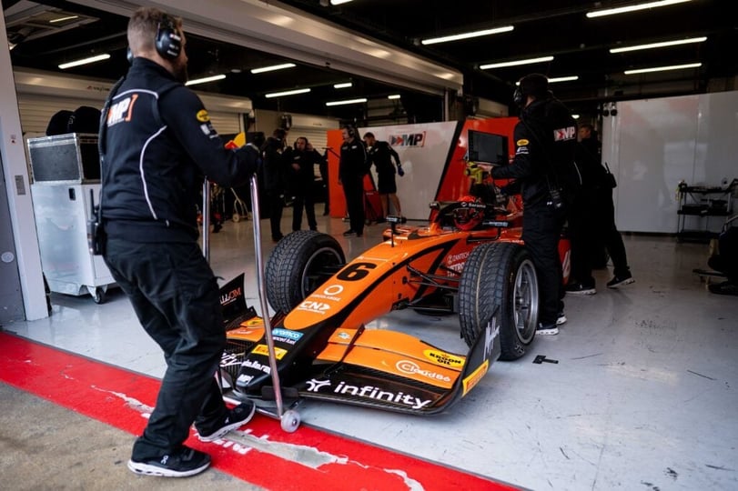 Teamleden verplaatsen een Formule 2-auto in de garage.