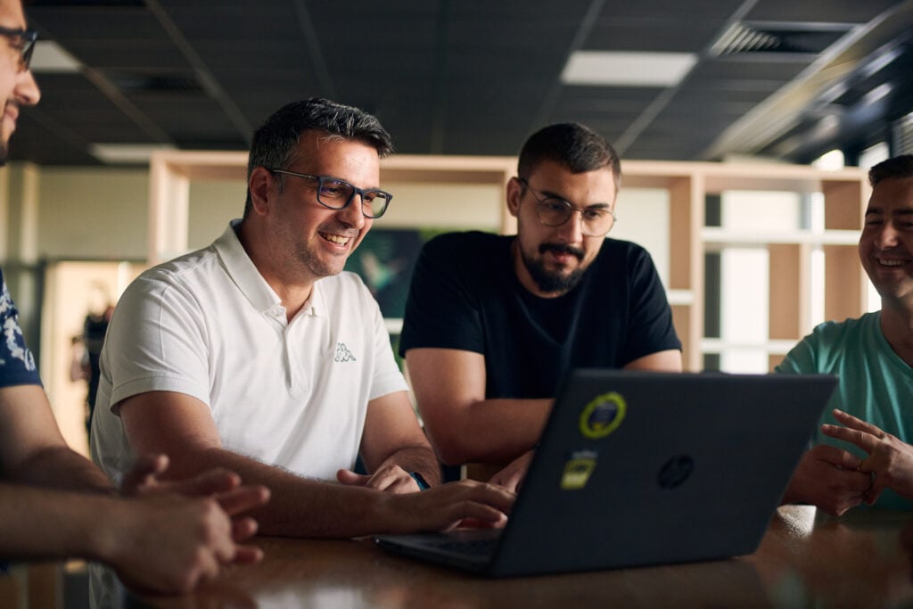Softwareontwikkelaars werken samen rond een laptop tijdens een teamsessie