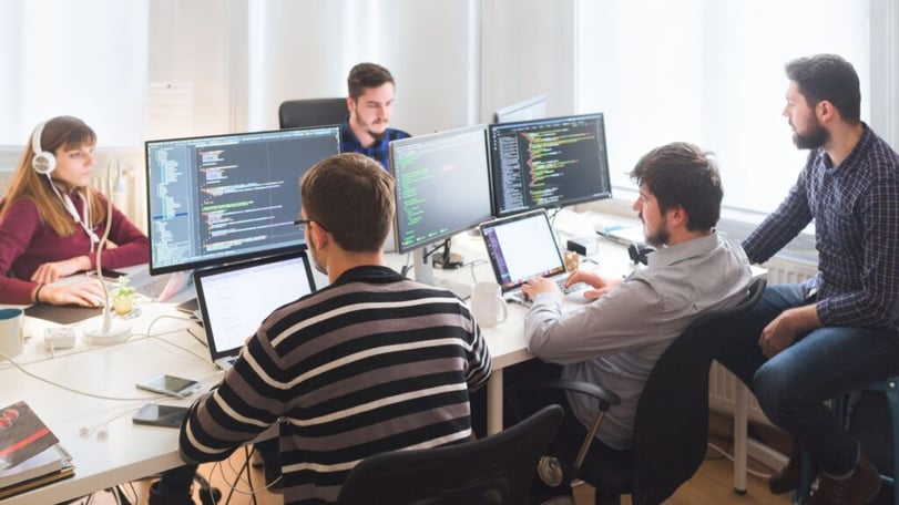 Softwareontwikkelaars werken samen achter meerdere beeldschermen