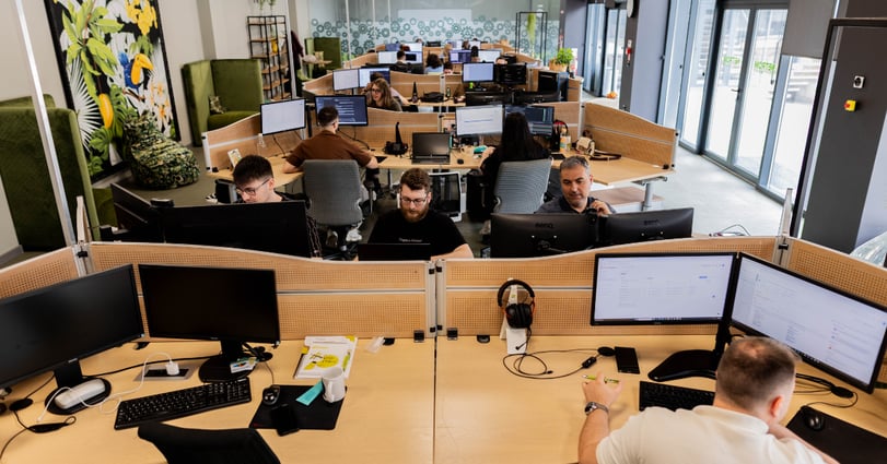 Softwareontwikkelaars werken achter meerdere beeldschermen in een gezamenlijke ontwikkelomgeving