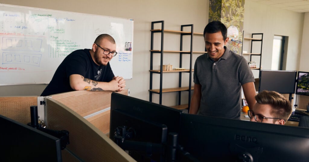 Drie NetRom Softwareontwikkelaars werken samen achter meerdere beeldschermen