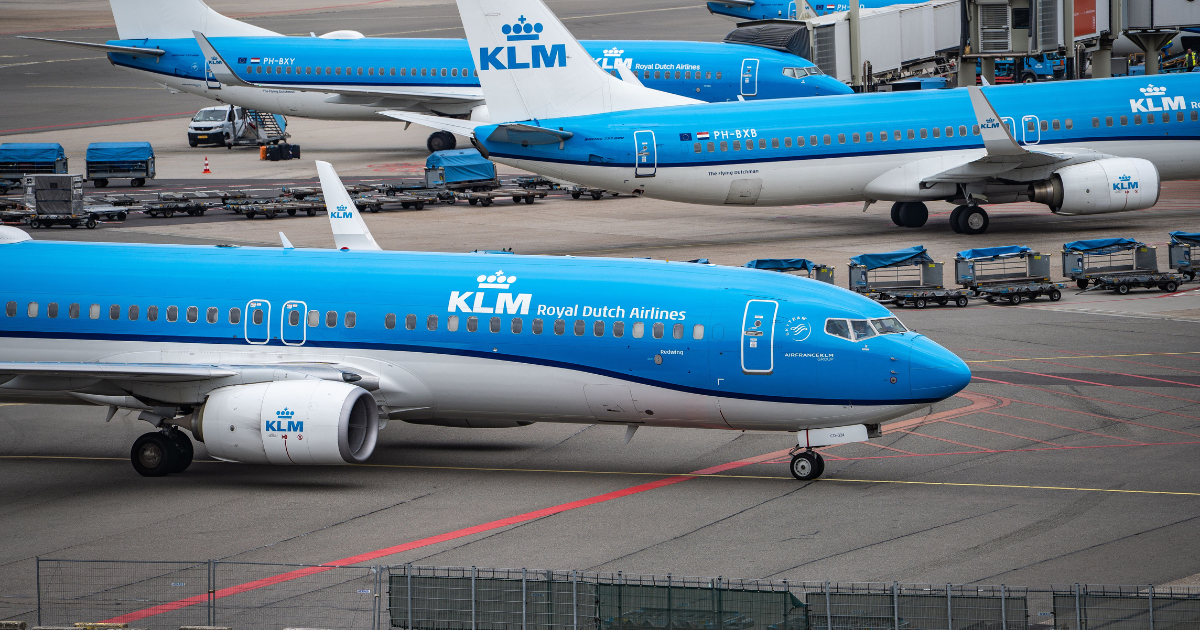 Blauwe KLM-vliegtuigen geparkeerd aan de gates op luchthaven Schiphol, gebruikt als visualisatie bij de column 'Chiphol of Schiphel?' van Han in 't Veld.