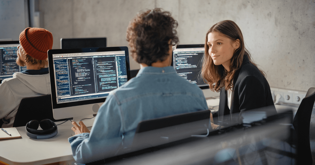 Softwareontwikkelaars in overleg voor een computerscherm met programmeercode, gebruikt als visualisatie van Developer Experience (DevEx) in software development.