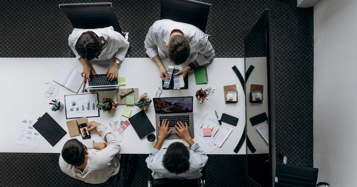 Bovenaanzicht van een agile projectteam dat samenwerkt aan een witte tafel met laptops, gebruikt als visualisatie bij het artikel over digitale transformatie en software outsourcing.