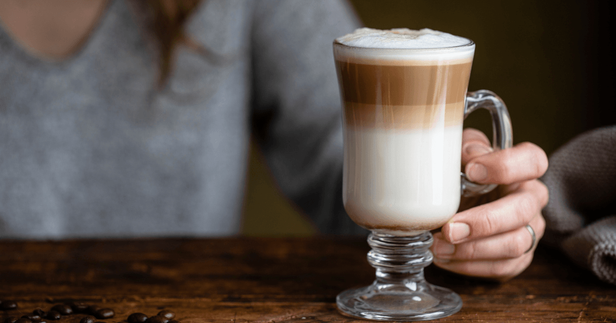 A glass of layered latte macchiato on a wooden table, illustrating the economic convergence between the Netherlands and Romania in Han in 't Veld's blog post.